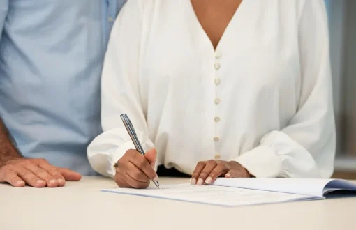 Young couple signing an apartment lease agreement with a property manager at a desk in a rental office.