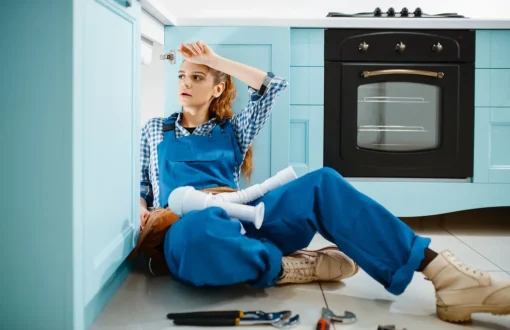 Maintenance technician sitting on a kitchen floor with plumbing tools during an unexpected repair situation